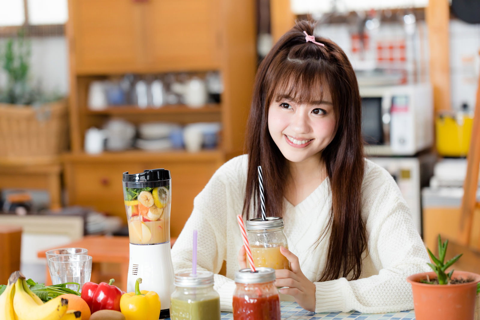 台所で自家製スムージーを飲む笑顔の女性［モデル：河村友歌］